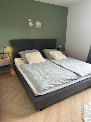 Ein Bett mit grauer Bettwäsche, einem dunklen Kopfteil und einem Nachttisch mit Lampe.