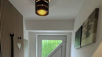 A hallway with a wooden slat wall, a round rug, a door with a triangular glass panel, and a ceiling light fixture.