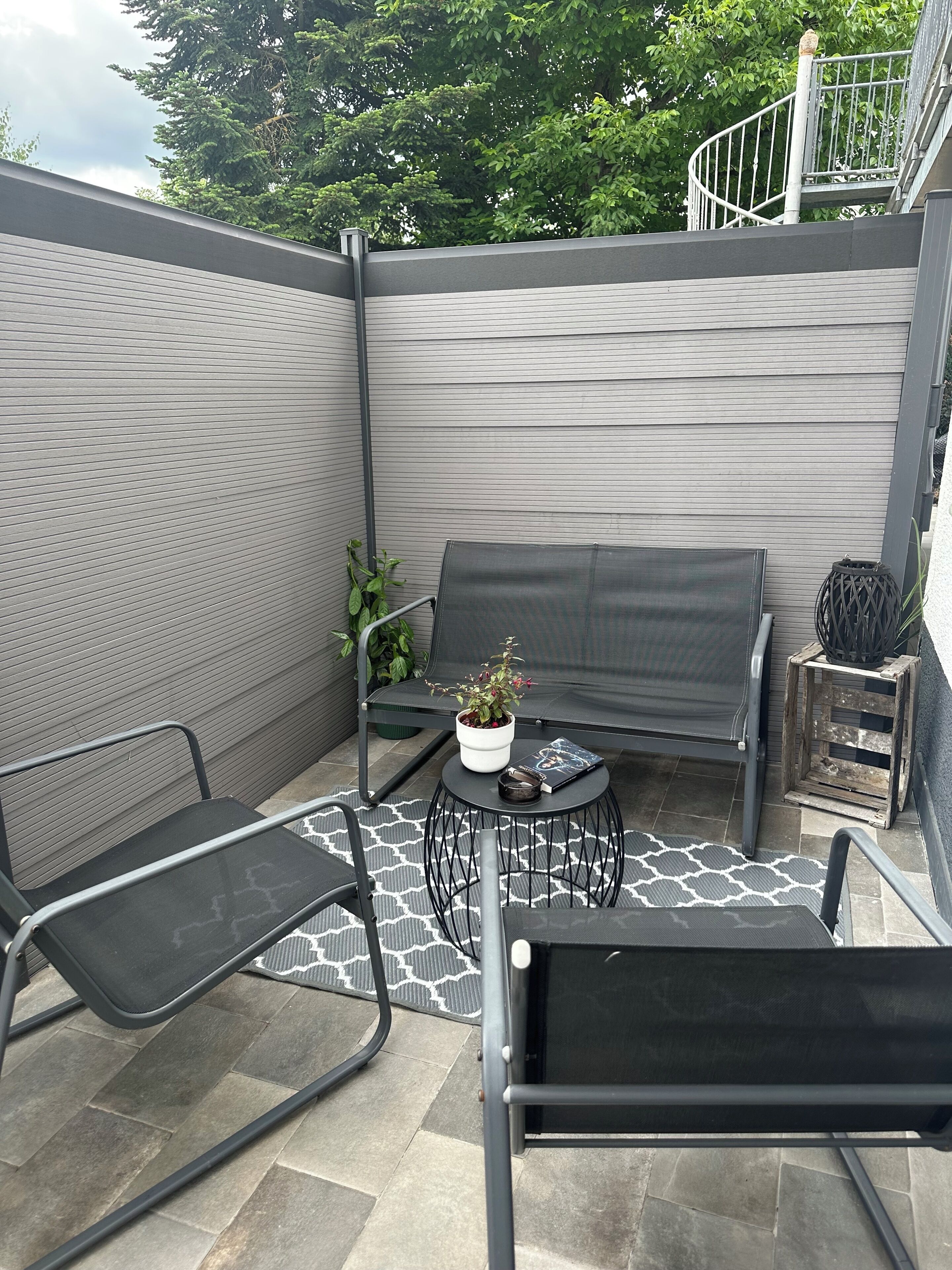 A patio with a sofa, chairs, a small table with a plant, and a decorative basket.