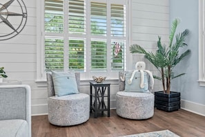 A room with two round ottomans, a small table, a potted plant, and a wall clock. - Captain's Lounge | Game Room, Chef's Kitchen, Sleeps 12 (Murrells Inlet)