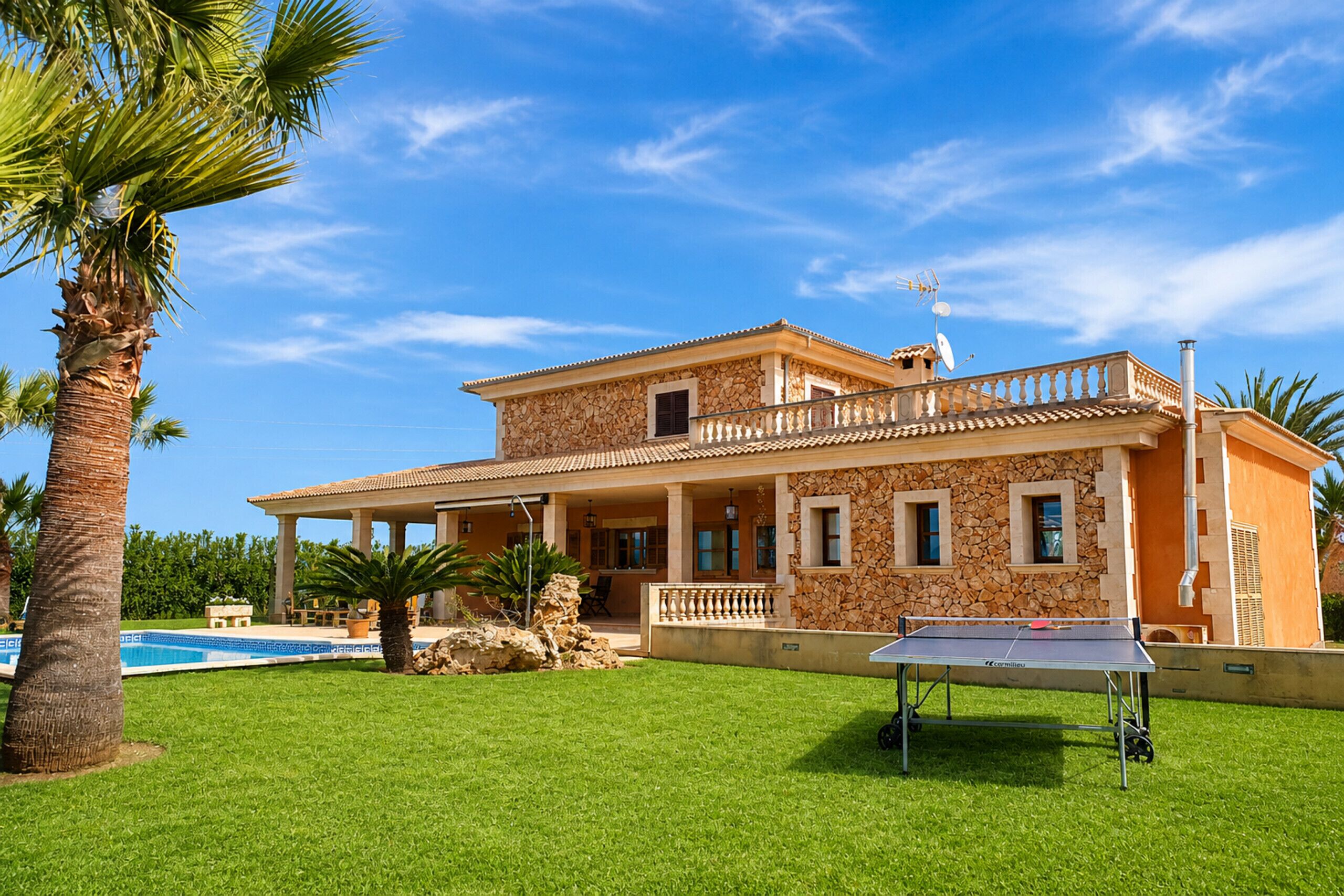 A two-story house with a stone facade, a swimming pool, and a ping pong table in the front yard.