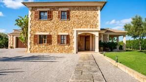 A stone building with a covered entrance, a gravel driveway, and a well-maintained lawn. - 283 Can Joan Verdal by Mallorca Charme (Muro)
