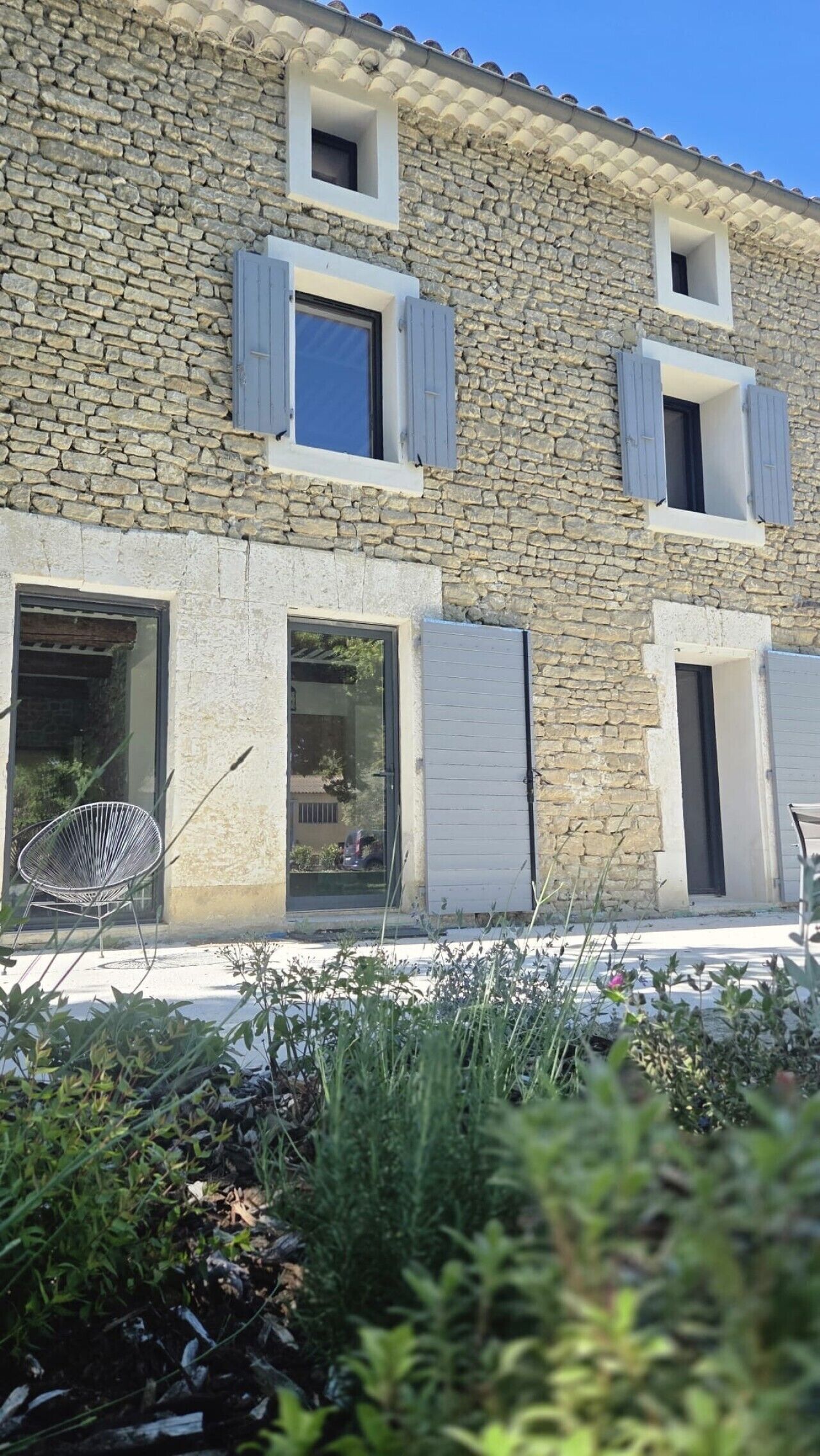 A stone building with multiple windows, some with shutters, and a chair outside.