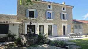A stone building with multiple windows, a stone fountain, and outdoor seating. - Le Mascalis | Large family home in Provence (L`Isle-sur-la-Sorgue)
