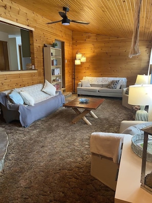 A cozy log cabin interior with a sofa, a coffee table, a bookshelf, and a lamp.