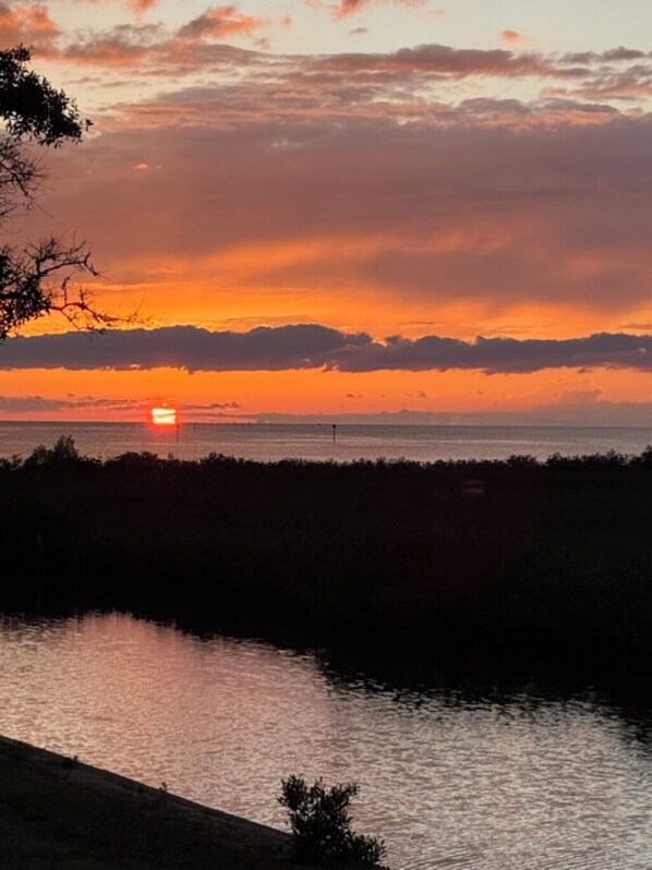 Un coucher de soleil sur une étendue d’eau, avec une côte lointaine à l’horizon.