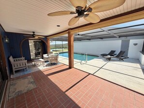 Un patio couvert avec une piscine, du mobilier d’extérieur et un ventilateur de plafond.