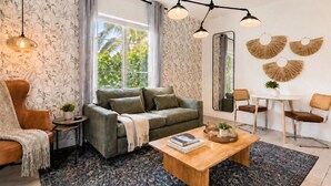 Una sala moderna con sofá, mesa de centro y sillones, un ventanal con cortinas y un espejo decorativo.