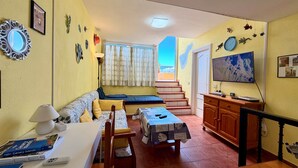 A living room with a sofa, a table, a lamp, a bookshelf, a staircase leading to a balcony, and a TV. - 2 BD Apartment with stunning view (Acantilados de los Gigantes)