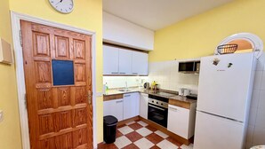 A kitchen with a wooden door, a clock, a microwave, and a refrigerator. - 2 BD Apartment with stunning view (Acantilados de los Gigantes)