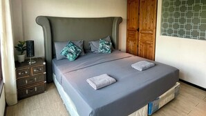 Een slaapkamer met een groot bed, een houten garderobe, een klein kastje en een potplant.