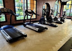 Ein Fitnessraum mit Laufbändern, Crosstrainern und Ergometer, die in einer Reihe angeordnet sind.