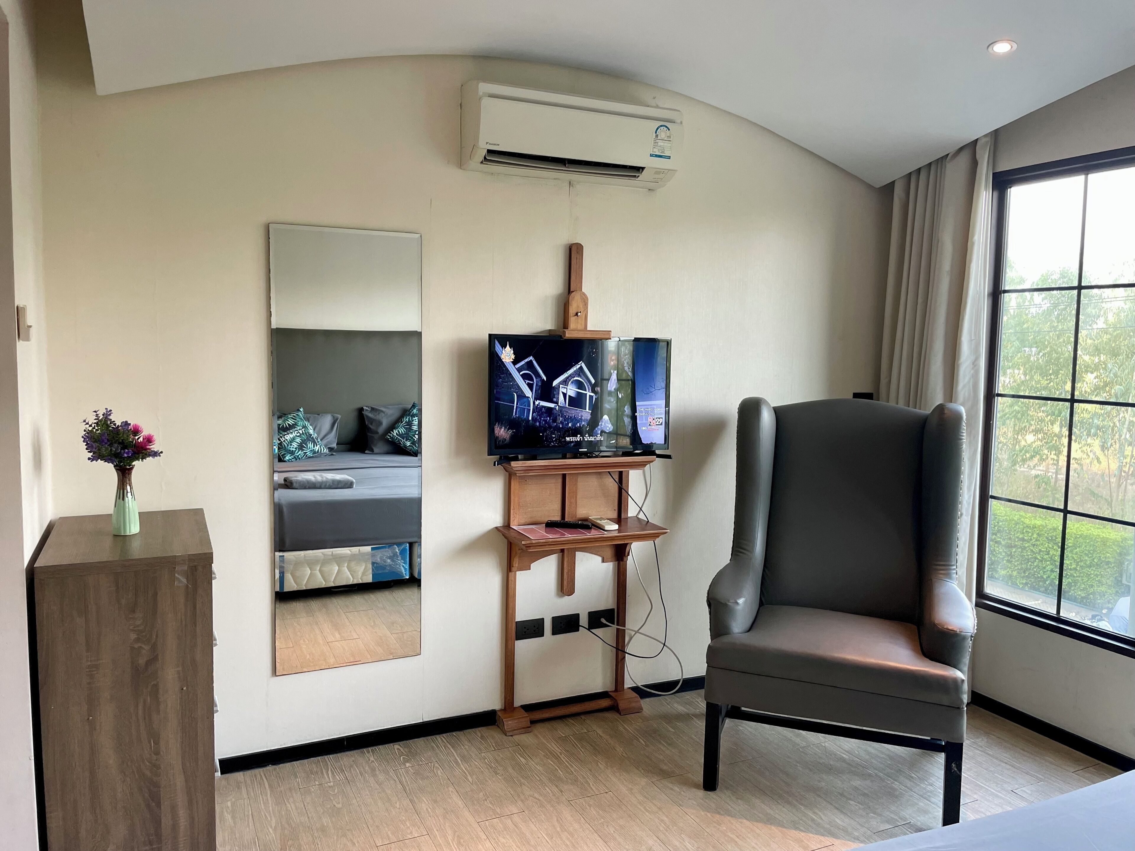 A hotel room with a flat-screen TV, a large mirror, a leather armchair, and an air conditioning unit.