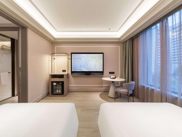 A hotel room with two beds, a desk, a chair, a TV mounted on the wall, and a window with curtains.