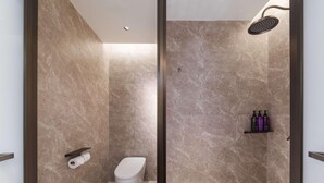 Un baño moderno con ducha, inodoro y estante con artículos de aseo.