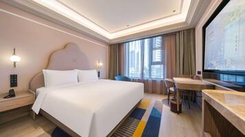 A hotel room with a large bed, bedside tables, a desk, a chair, a television, and a window with curtains.