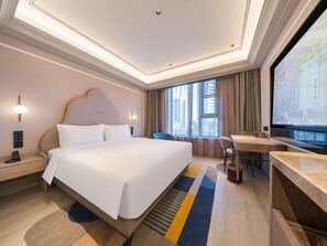 A hotel room with a large bed, bedside tables, a desk, a chair, a television, and a window with curtains.