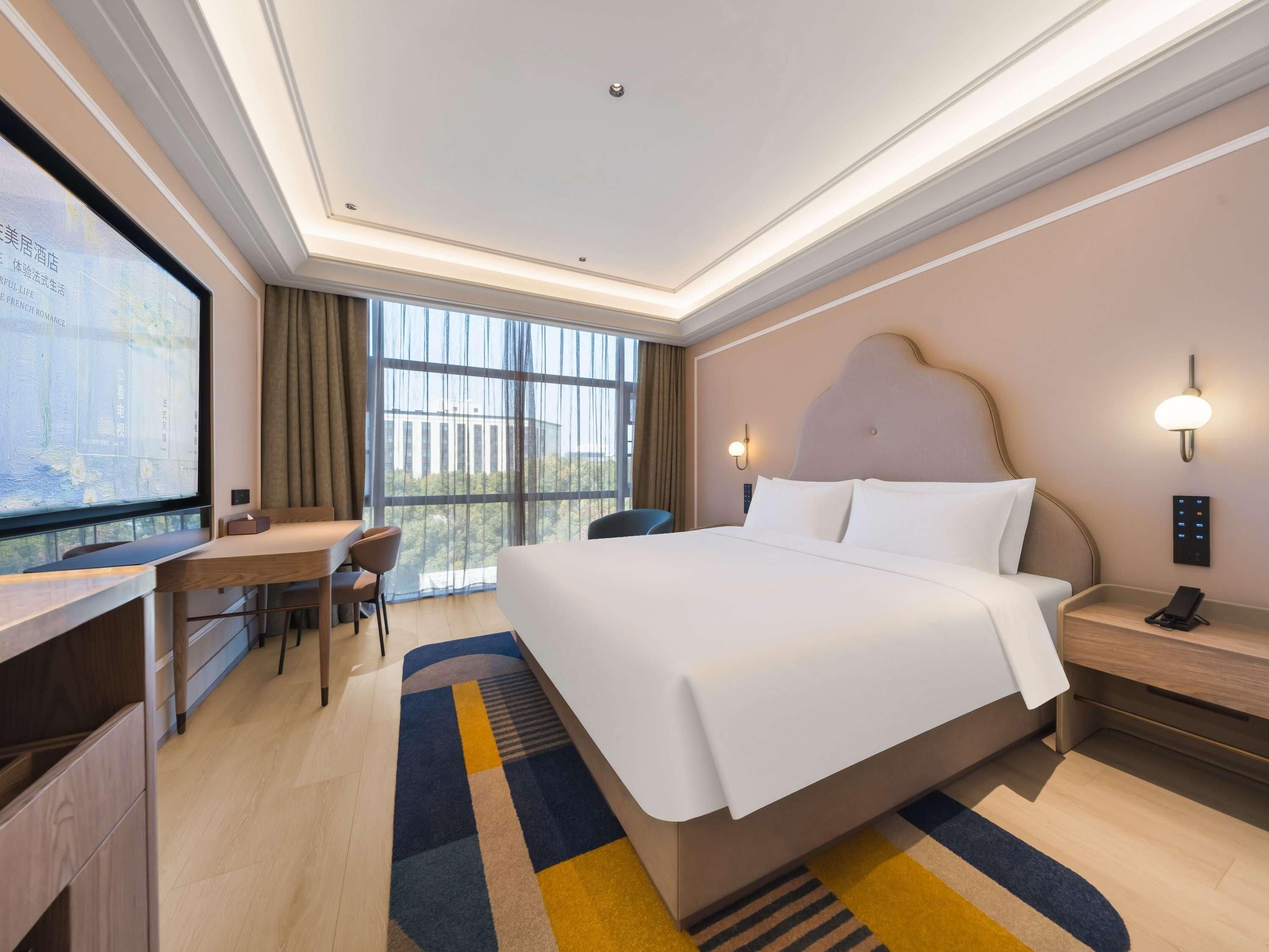 A hotel room with a large bed, a desk with a chair, a television, and a view of the outdoors.