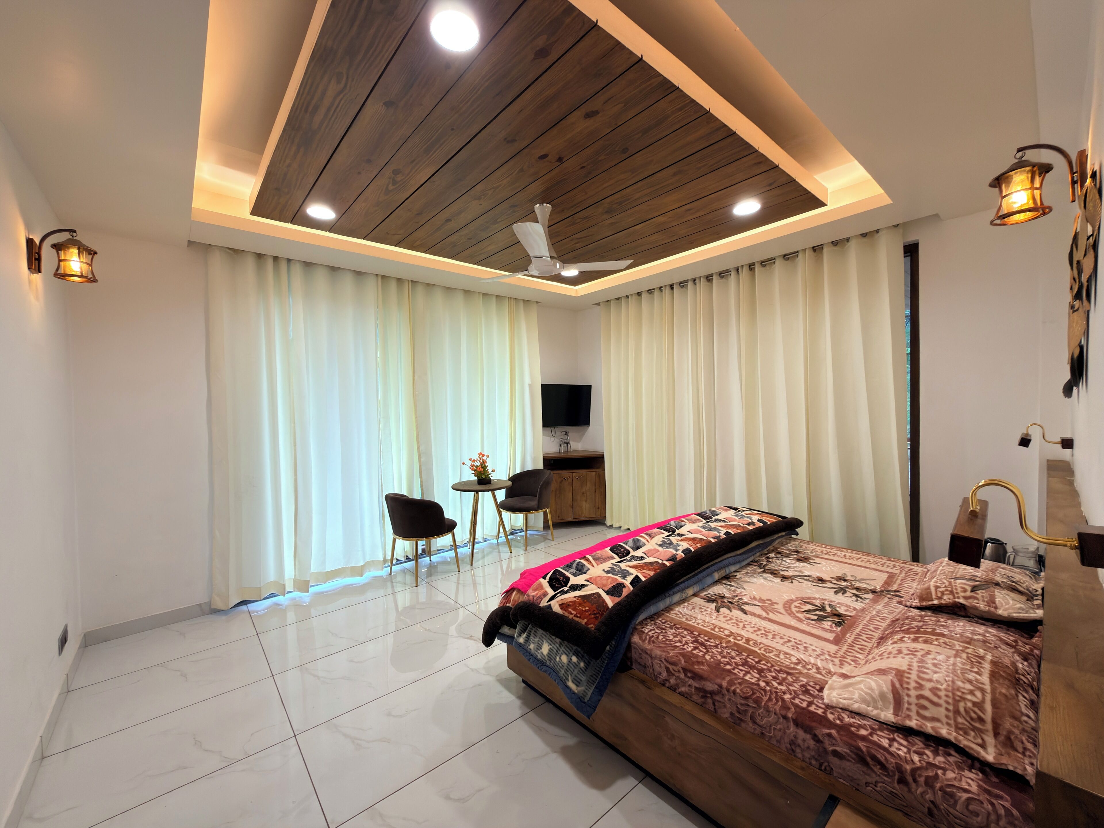 A modern bedroom with a wooden ceiling, a bed with patterned bedding, a desk with a chair, and a television.