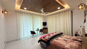 A modern bedroom with a wooden ceiling, a bed with patterned bedding, a desk with a chair, and a television.