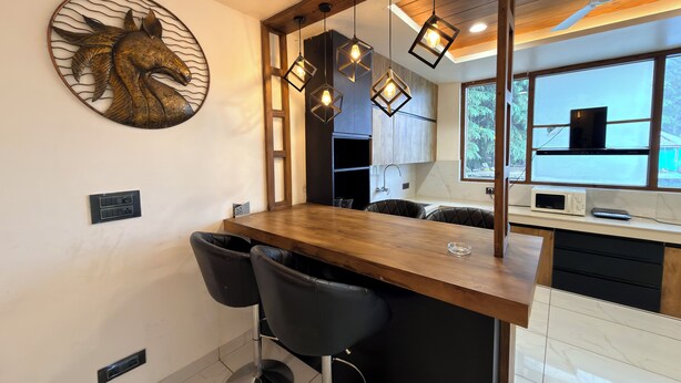 Une cuisine moderne avec un îlot central en bois, des tabourets de bar noirs, des luminaires suspendus et un élément décoratif mural.