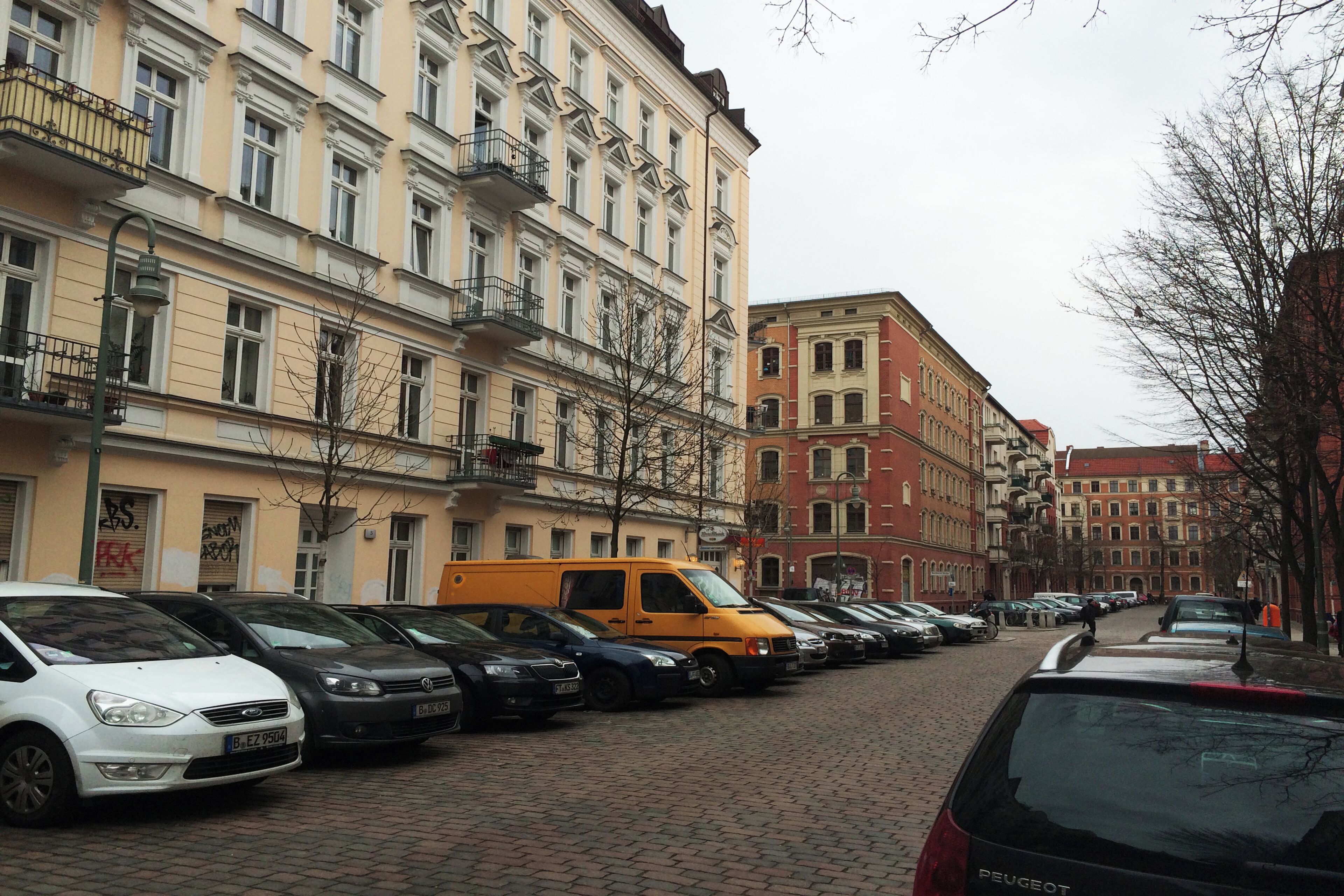 A street lined with parked cars and multi-story buildings with balconies.