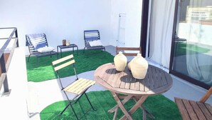 Eine kleine Terrasse im Freien mit einem runden Holztisch, zwei Stühlen und einem Klappstuhl.