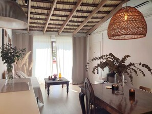 A dining area with a wooden table, chairs, a hanging light fixture, and a view of the outdoors through a window. - Apartment with terrace 5 minutes from the historic center (Alicante)