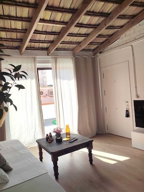 A room with a wooden ceiling, a white door, a small table with a remote control, and a plant. - Apartment with terrace 5 minutes from the historic center (Alicante)