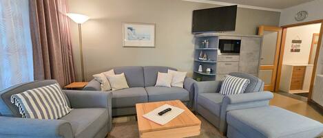 A living room with a sofa set, a coffee table, and a flat-screen TV mounted on the wall.