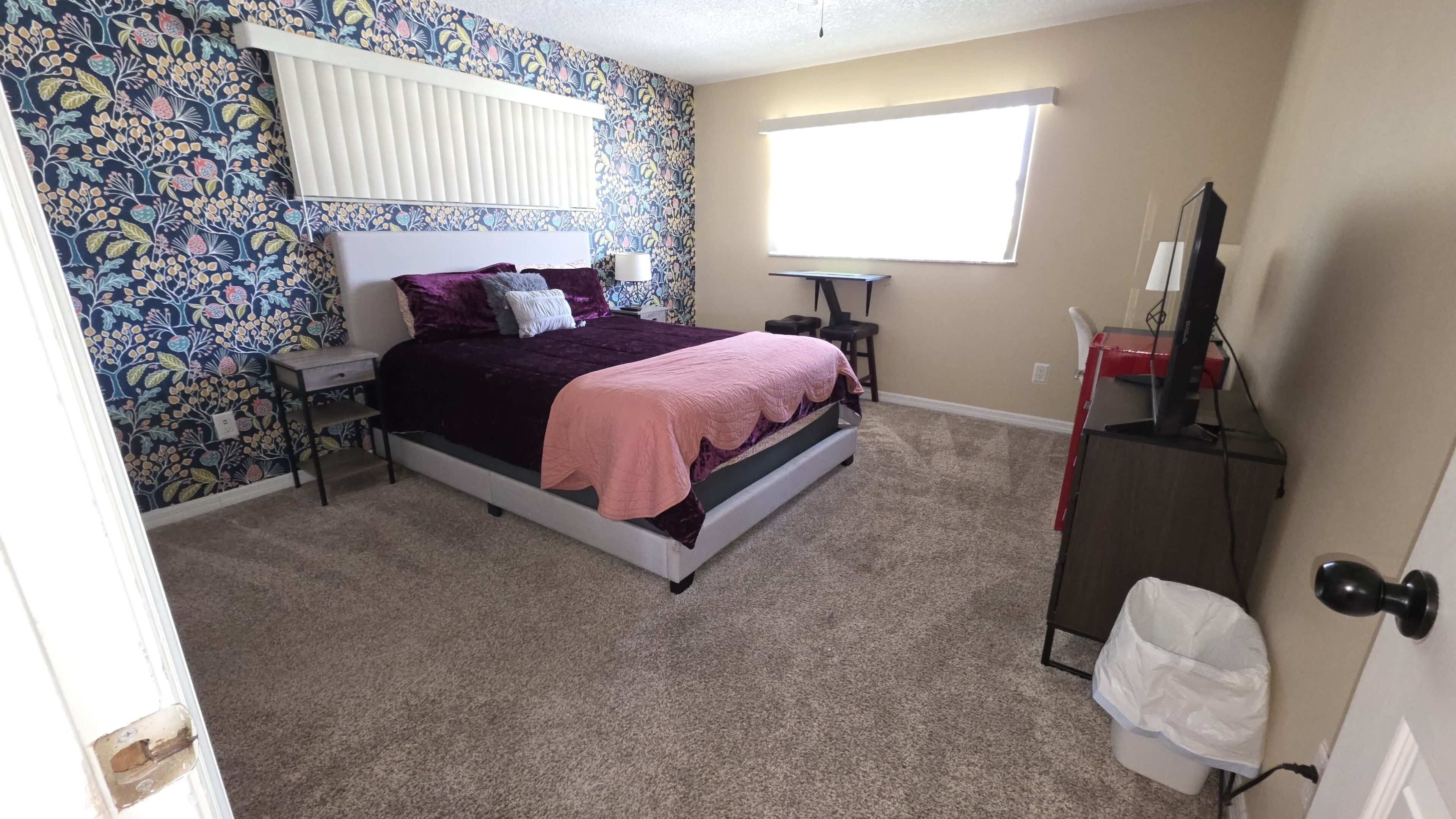 A bedroom with a bed, a nightstand, a dresser, a window, and a door.