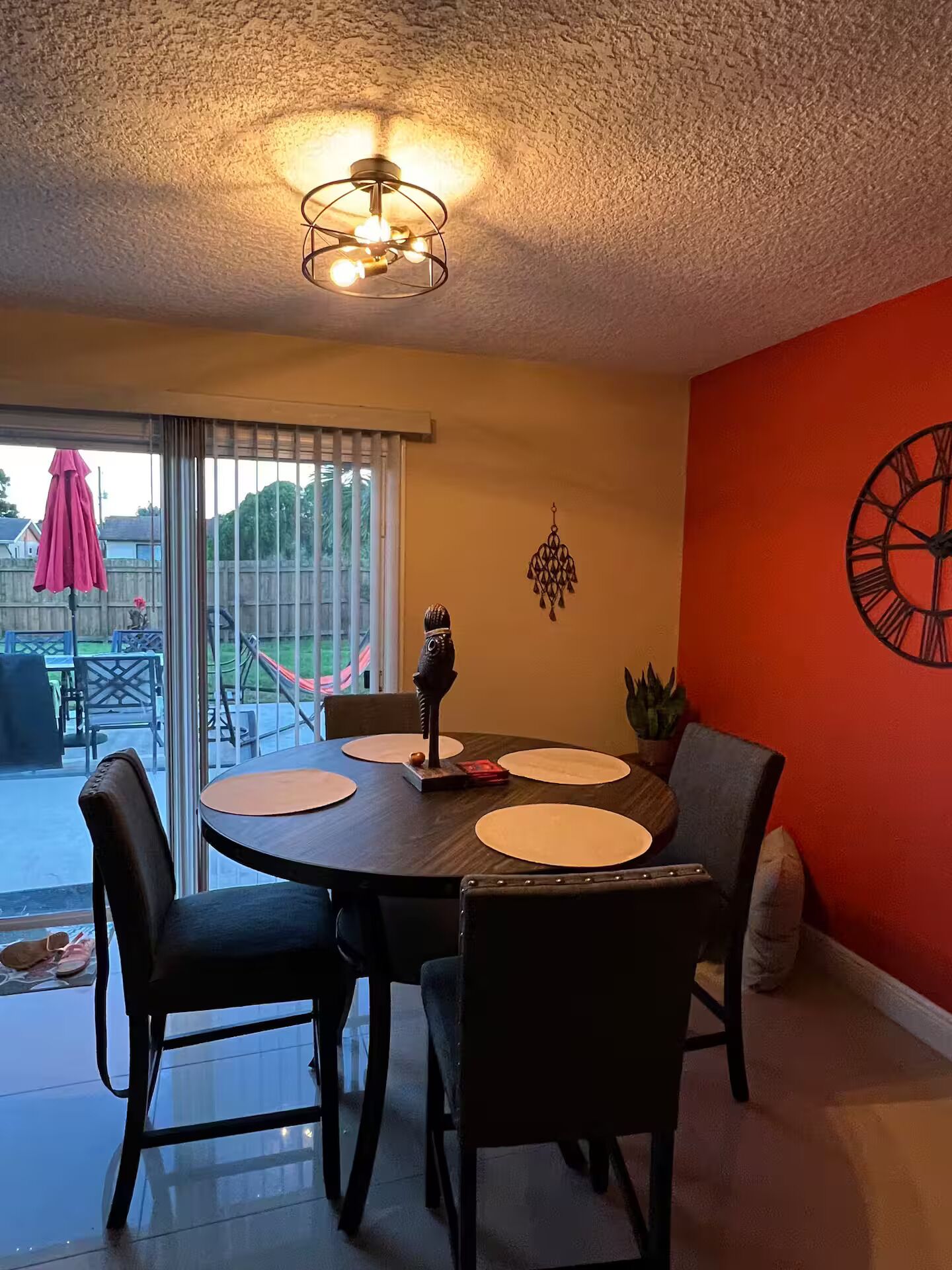 A dining area with a round table, chairs, a wall clock, and a ceiling light fixture.