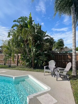 Ein Garten mit Swimmingpool, weißen Adirondack-Stühlen und üppiger tropischer Bepflanzung.