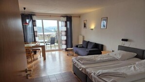 Habitación de hotel con cama, sofá, mesa de comedor con sillas y vistas a través de un ventanal.