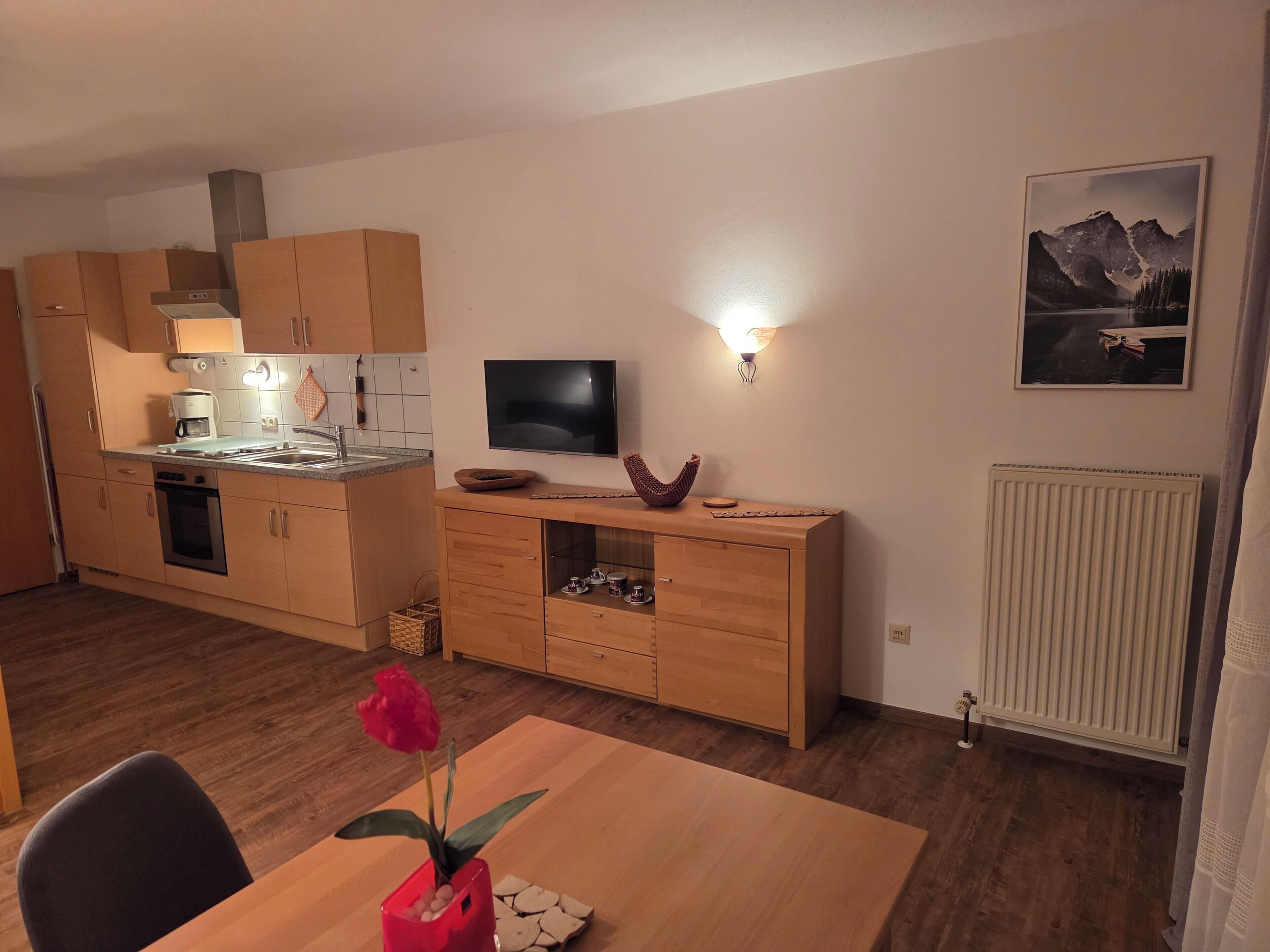 A modern kitchen with wooden cabinets, a built-in oven, and a dining area with a table and chairs.