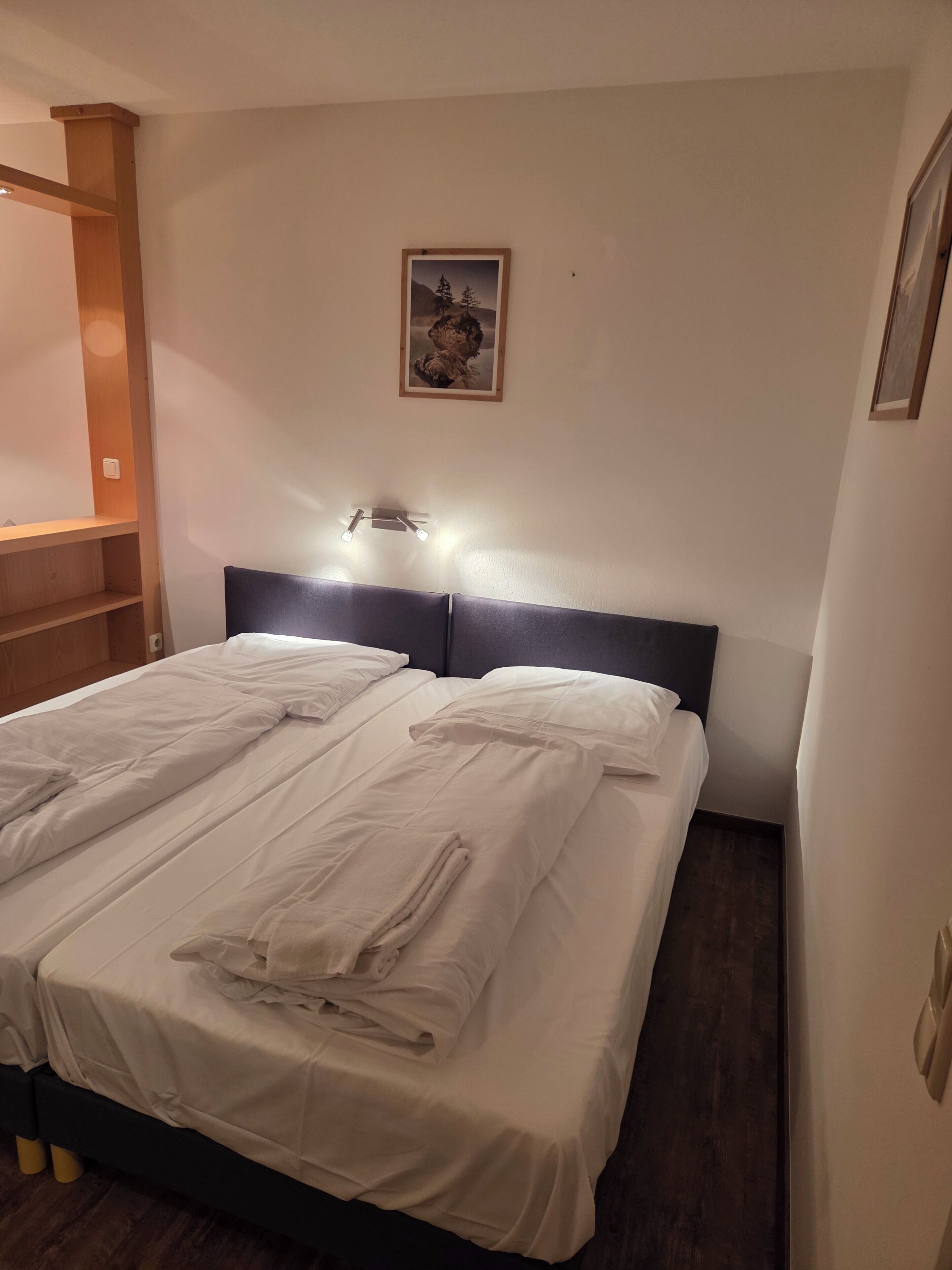 A hotel room with a double bed, a headboard, a wall-mounted light fixture, and a framed picture.