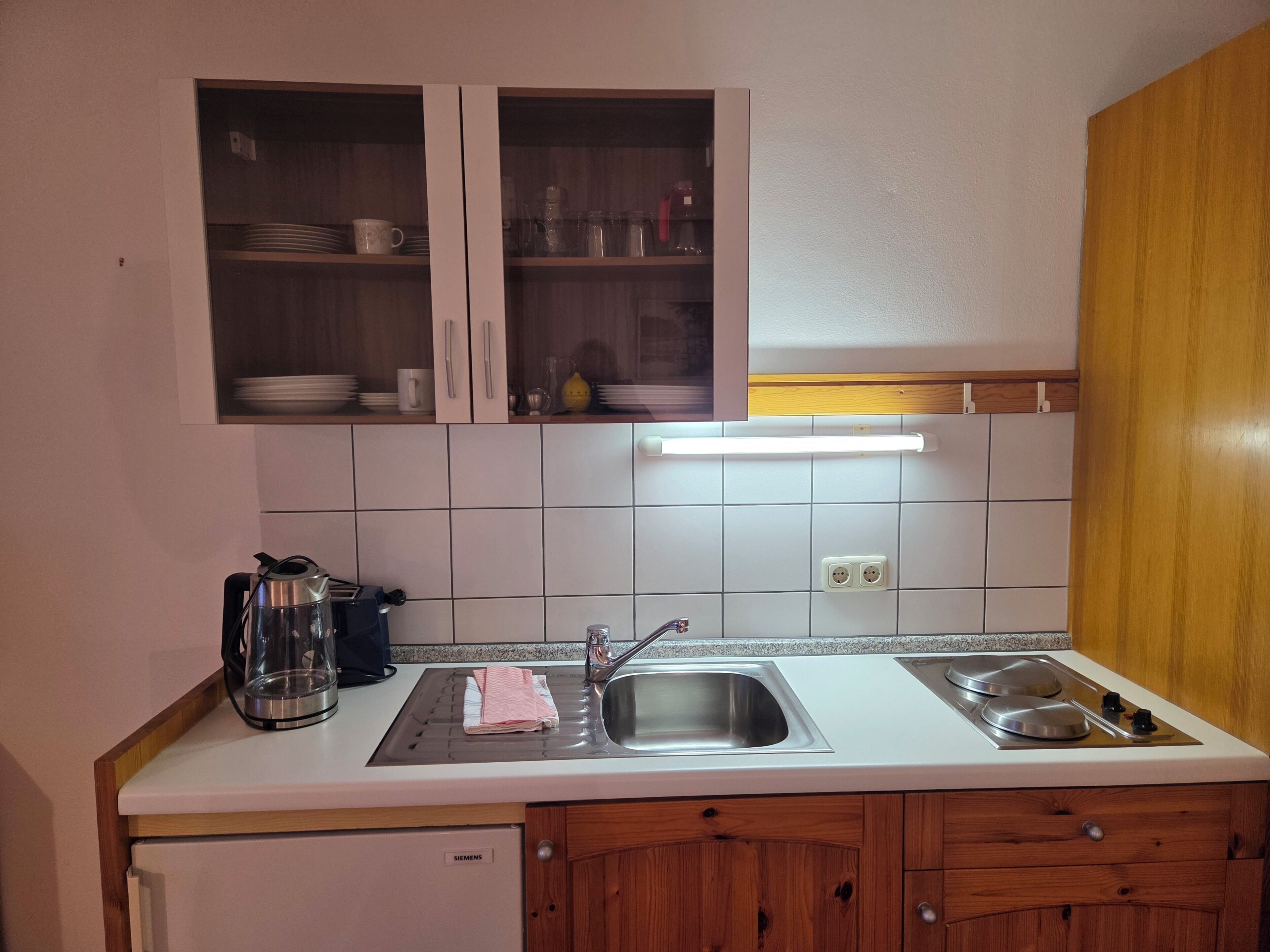 A kitchen with a Siemens refrigerator, a double sink, and wooden cabinets.