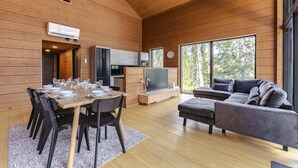 A modern interior with a dining area, sofa, TV, and large windows.