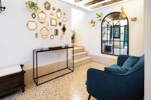 A room with a blue sofa, a glass-top table, a wooden bench, a staircase, and a wall decorated with mirrors and plants. - Your Private Garden - Cà de l'Astrologo (Venezia)