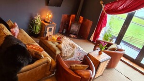 A cozy living room with a sofa, a side table with a vase, a fireplace, and a large window with a view of greenery. - The View, Luxury Retreat, Outstanding views over the countryside & Hebden Bridge (Cragg Vale)