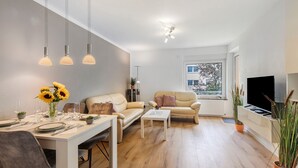 A modern living room with a dining area, wooden flooring, and a large window providing a view of the outside. - Apartment 'Melody' with Balcony and Wi-Fi (Oberkochen)
