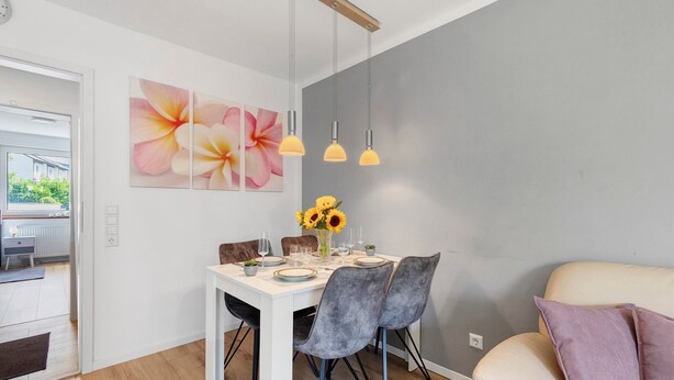 A dining area with a white table, grey chairs, and a vase of sunflowers. - Apartment 'Melody' with Balcony and Wi-Fi (Oberkochen)