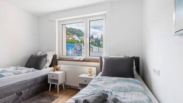 A bedroom with a bed, bedside tables, a radiator, and a window with a view of houses.