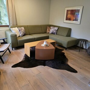 Un salon avec un canapé vert, une table basse ronde, un tapis noir à poils longs et une petite table ronde.