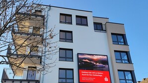 Un edificio de varios pisos con un gran anuncio digital, una tienda con letrero 'Amax' y un árbol en primer plano.