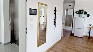 Un pasillo con una puerta marcada '2L', un espejo, un cuchillo en la pared, una mesita y un refrigerador.