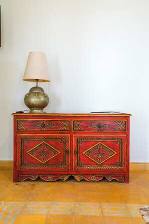 Un buffet rouge orné de motifs complexes, une lampe posée sur le dessus et un sol à motifs.