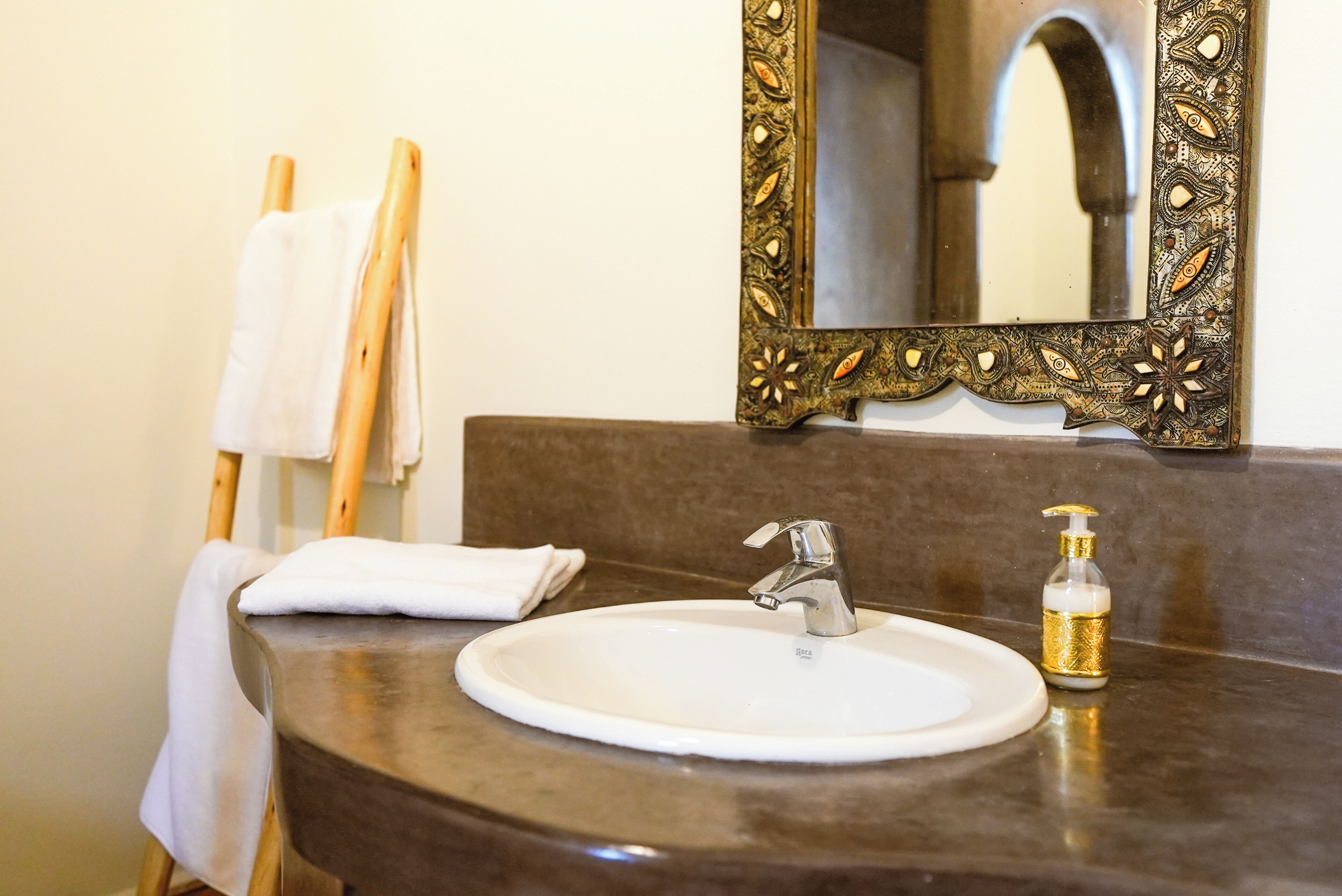 A bathroom with a round sink, a mirror with ornate frame, and a towel rack.