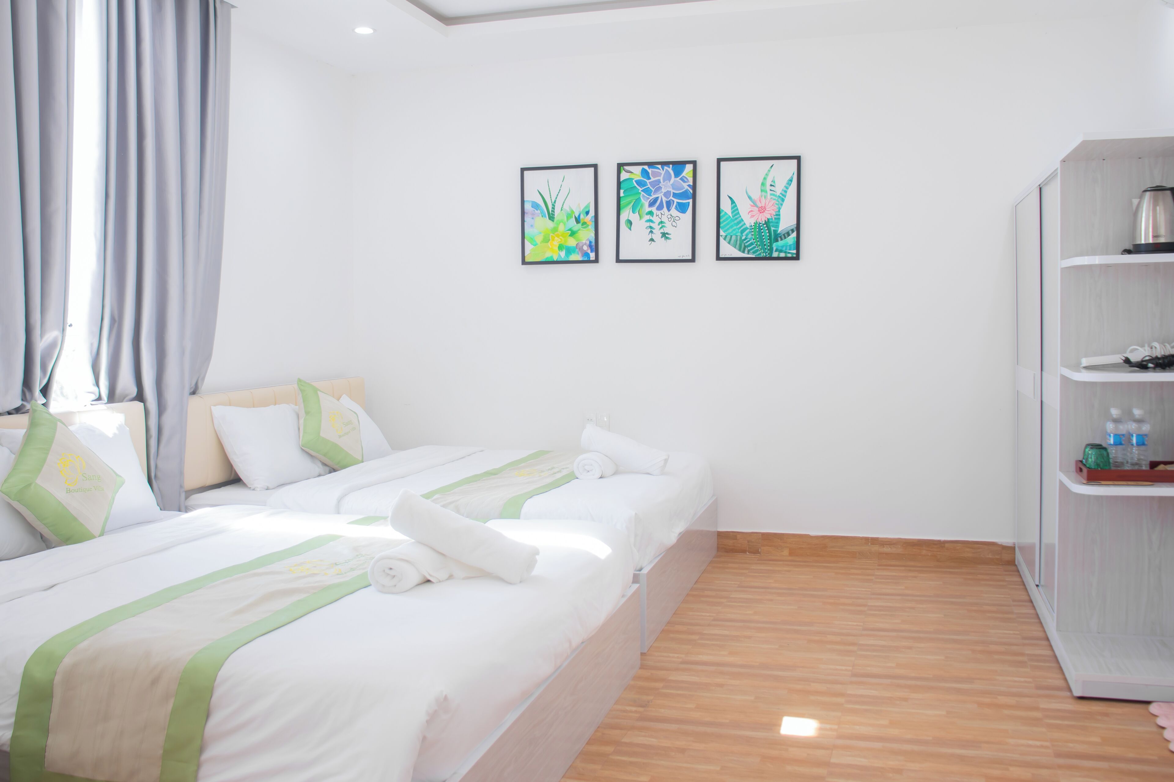 Ein Hotelzimmer mit zwei Betten, einem Kleiderschrank und drei gerahmten Kunstwerken an der Wand.