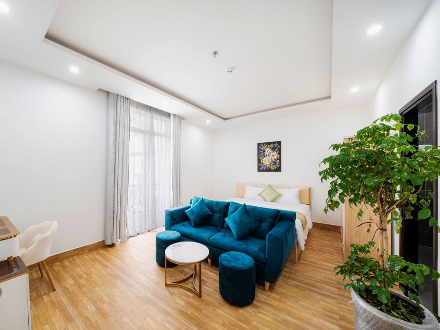 Una habitación moderna con un sofá azul, una mesa redonda, una cama, un escritorio con computadora y una planta en maceta.